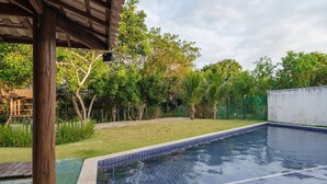 A swimming pool with a tiled edge, surrounded by a grassy area and trees. - Comfortable apt With Pool Near the Beach Vrl0002 (Camaçari)