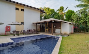 A swimming pool with a tiled deck, a covered outdoor seating area, and a building with a tiled roof. - Comfortable apt With Pool Near the Beach Vrl0002 (Camaçari)