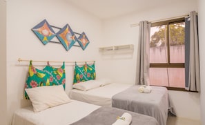 Una habitación con dos camas, un ventanal con cortinas y una pared con tres cuadros de peces.