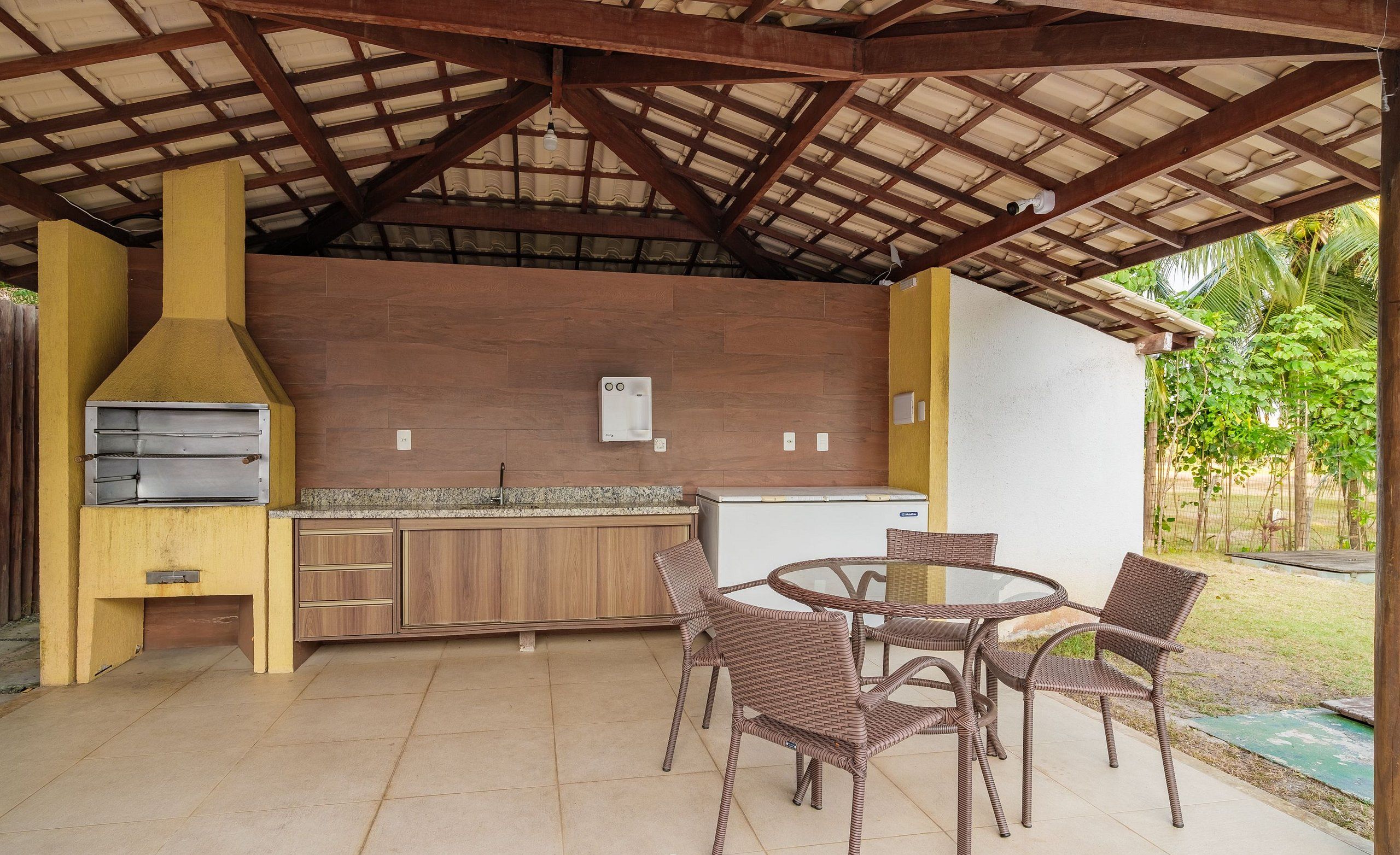Un área de cocina exterior con una parrilla, un refrigerador y un juego de comedor.