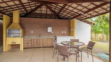 Un área de cocina exterior con una parrilla, un refrigerador y un juego de comedor.