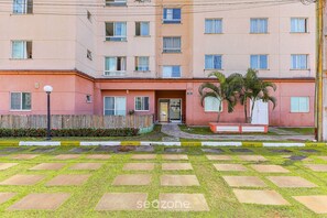 A multi-story residential building with a flat facade, a central entrance, and a small garden area with palm trees. - Condominium With a Pool 850m From Praia do Sul, Ilheus/ba VGT (Ilhéus)
