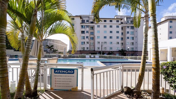 A pool area with palm trees, a sign indicating pool rules, and a building in the background. - Condominium With a Pool 850m From Praia do Sul, Ilheus/ba VGT (Ilhéus)