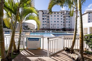 A pool area with palm trees, a sign indicating pool rules, and a building in the background. - Condominium With a Pool 850m From Praia do Sul, Ilheus/ba VGT (Ilhéus)