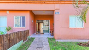 A building with a pink facade, a wooden fence, and a small garden area. - Condominium With a Pool 850m From Praia do Sul, Ilheus/ba VGT (Ilhéus)