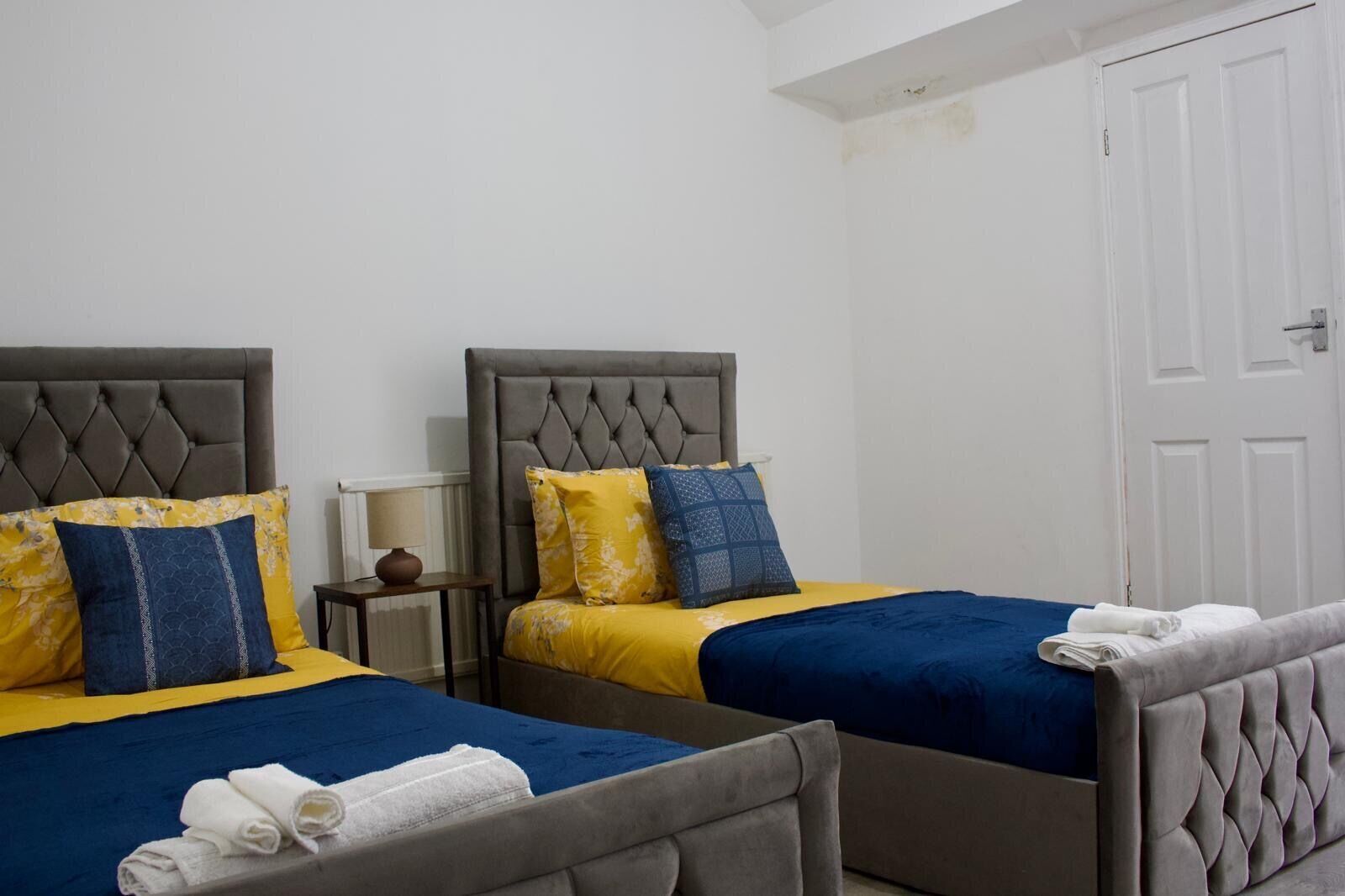 A hotel room with two beds, each with a tufted headboard, and a white door.