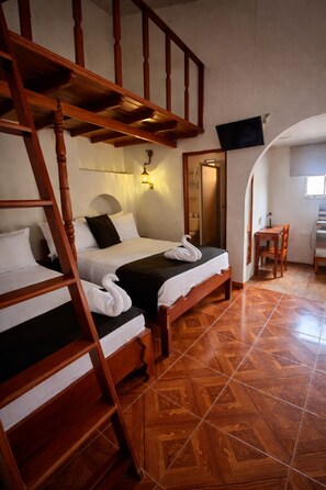 A room with two wooden bunk beds, a desk, a chair, and a television mounted on the wall. - Hotel Época (Belen)