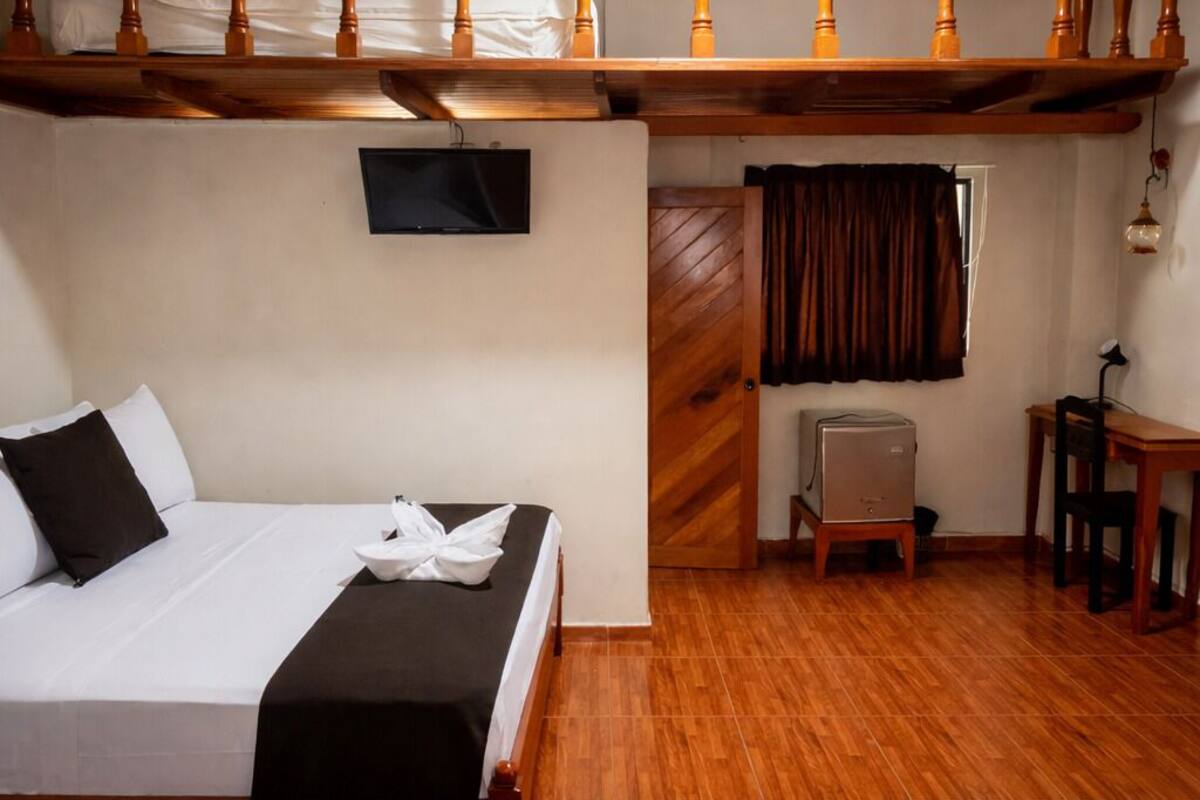 A hotel room with two beds, a TV, a wooden ceiling, and a small table with a lamp.