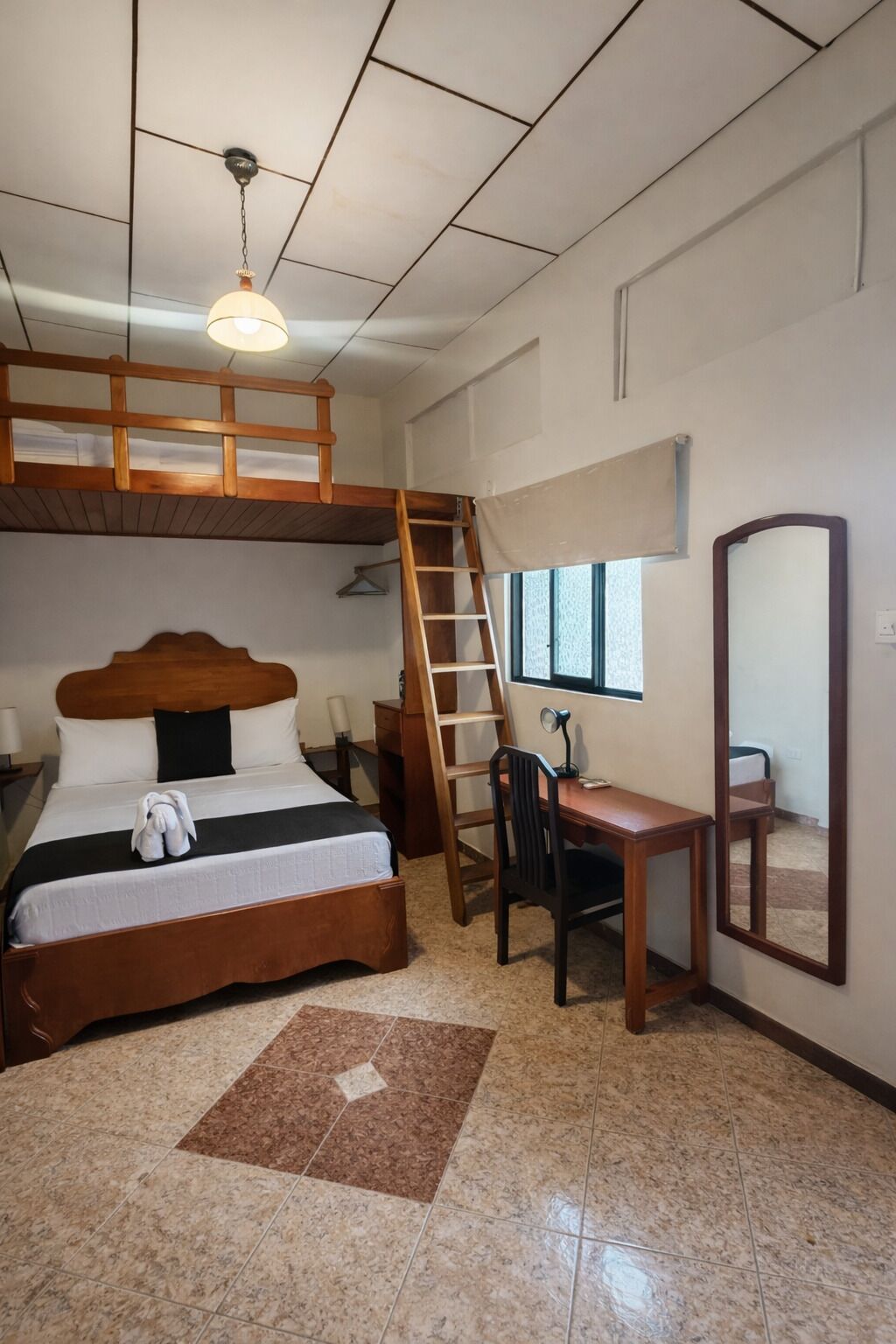 A bedroom with a bunk bed, a desk, a chair, a ladder, a mirror, and a hanging light fixture.