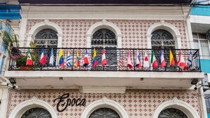 Un edifici amb tres finestres d'arc, un balcó amb banderes i el nom 'Epoça' a la façana.