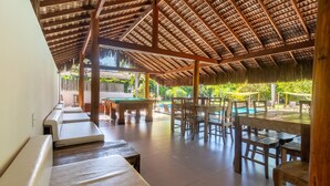 Un espacio al aire libre cubierto con piscina, muebles de madera y techo de paja.