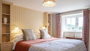 A bedroom with a large bed, bedside lamps, a window with curtains, and built-in shelving with decorative items.