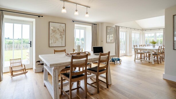 A spacious dining area with a long table, wooden chairs, and a laptop on the table.