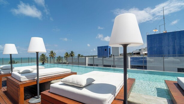 A rooftop pool area with lounge chairs and lamps, overlooking a clear blue sky and ocean. - SYH - Complete Beachfront Condominium in Cabo Branco/pb (João Pessoa)