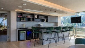 A modern kitchen with a bar area, built-in shelves, and a large window offering a view of the outdoors. - SYH - Complete Beachfront Condominium in Cabo Branco/pb (João Pessoa)