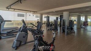 A gym with exercise equipment, large windows, and a wooden floor. - SYH - Complete Beachfront Condominium in Cabo Branco/pb (João Pessoa)