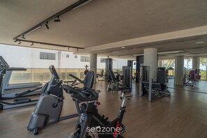 A gym with exercise equipment, large windows, and a wooden floor.