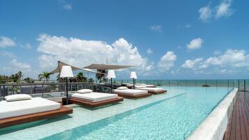 A pool area with lounge chairs and umbrellas, overlooking a clear blue sky and ocean.