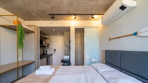 Une chambre d’hôtel moderne dotée d’un grand lit, d’une petite kitchenette, d’une salle de bain avec un mur en marbre et d’un climatiseur fixé au plafond.