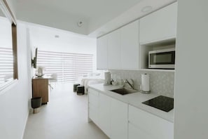 Una cocina moderna con muebles blancos, un microondas integrado y un amplio ventanal con persianas.