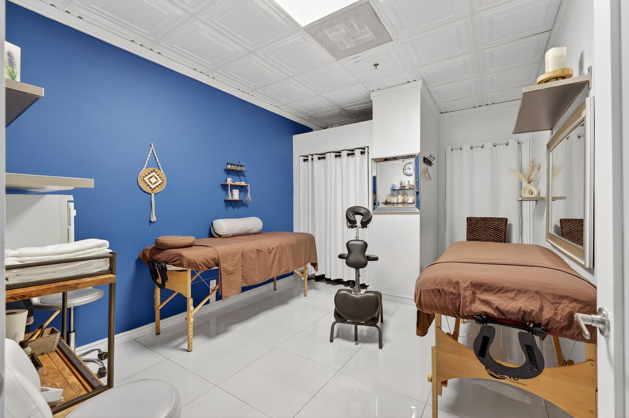 Ein Zimmer mit zwei Betten, einem Massagesessel, einem Ablagefach für Pflegeprodukte und einem Fenster mit Vorhängen.