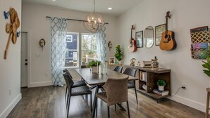 A dining area with a wooden table, chairs, and a chandelier. There are guitars and framed pictures on the walls.