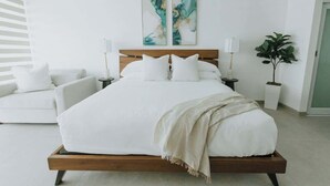 A modern bedroom with a wooden bed, white bedding, and two abstract paintings on the wall.