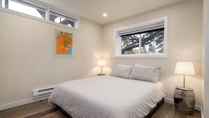 A bedroom with a bed, two bedside lamps, a window, and a wall-mounted abstract painting. - Chic Downtown Steamboat Condo – Walk to Prime Spots (Steamboat Springs)