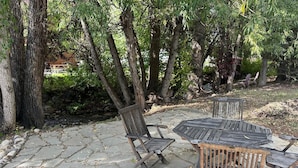 An outdoor patio with stone flooring and wooden furniture, surrounded by trees and greenery. - Chic Downtown Steamboat Condo – Walk to Prime Spots (Steamboat Springs)