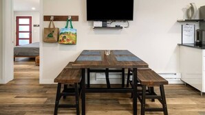 A room with a wooden dining table and benches, a flat-screen TV mounted on the wall, and a kitchen area with white cabinets. - Chic Downtown Steamboat Condo – Walk to Prime Spots (Steamboat Springs)