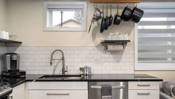A modern kitchen with white cabinets, a black countertop, a stainless steel sink, and hanging pots. - Chic Downtown Steamboat Condo – Walk to Prime Spots (Steamboat Springs)