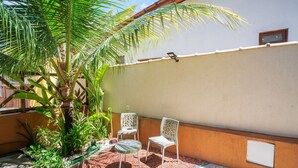 A patio area with two white chairs, a small table, and a palm tree. - Cozy Studio in Praia do Forte Vgc0005 (Mata de São João)