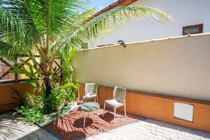 Un patio con dos sillas blancas, una mesita y una palmera.