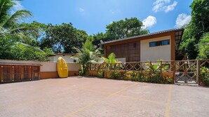 A courtyard with a tiled floor, a yellow inflatable pool, and a building with a brown roof and windows. - Cozy Studio in Praia do Forte Vgc0005 (Mata de São João)