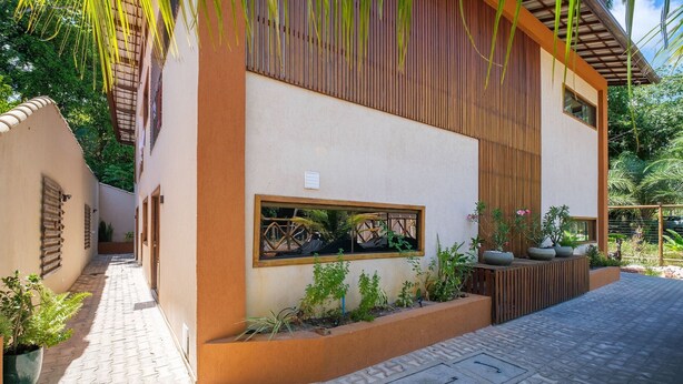 A modern building with a beige facade, wooden slats, and a small window. - Cozy Studio in Praia do Forte Vgc0005 (Mata de São João)