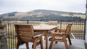 Een houten tafel en stoelen op een balkon, met uitzicht op glooiende heuvels.