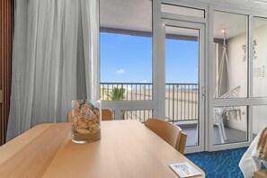 A room with a large window, a glass table with a decorative item, and a view of the outside. - ESJ Beach Studio | 2 Queen Beds + Workstation (Carolina)