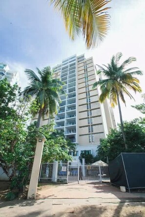 A tall building with a modern design, surrounded by greenery and palm trees. - ESJ Beach Studio | 2 Queen Beds + Workstation (Carolina)