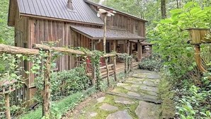 Un chalet rustique en bois, doté d’un toit en métal, d’un chemin de pierre menant à l’entrée et d’une clôture en bois ornée de plantes grimpantes.