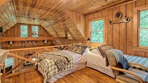 Une chambre rustique dans un chalet, avec un lit en mezzanine, une chaise et une fenêtre donnant sur la forêt.