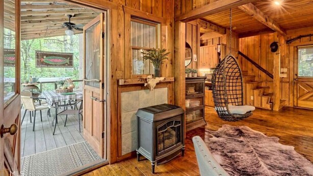 Un intérieur de chalet chaleureux, avec un revêtement en bois, une cheminée, un fauteuil suspendu et un coin repas offrant une vue sur la forêt.