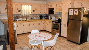 A kitchen with white cabinets, a stainless steel refrigerator, a microwave, and a dining table with chairs. - Historic Cozy Cabin Downtown Del Rio (Del Rio)