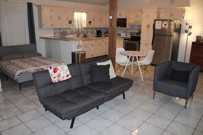 Un espacio habitable compacto con sofá, sillón, cama, mesita y kitchenette.