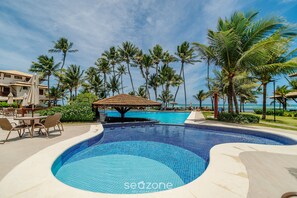 A swimming pool with a tiled edge, surrounded by palm trees and a building with a tiled roof.