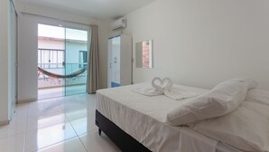 Una habitación de hotel con una cama, un ventanal corredero que da a un balcón y un equipo de aire acondicionado.