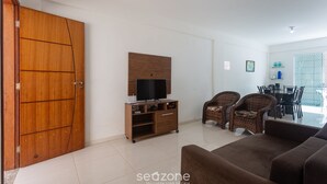Una sala de estar con sofá, sillas de mimbre, un mueble para televisión y un comedor con sillas y mesa.
