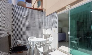 A small outdoor patio with a checkered wall, a grill, and white plastic furniture.