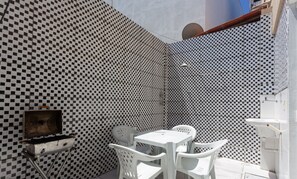 A patio area with a checkered wall, a grill, and white plastic chairs.