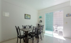 A dining area with a rectangular table and six chairs, a small shelf with items, and a door leading to an outdoor area with a patterned fence. - Townhouse 300m From Ilheus Beach Vcm005 (Ilhéus)