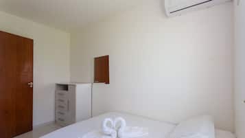 Una camera d'albergo con un letto, una porta in legno, una cassettiera bianca e un condizionatore d'aria a parete.